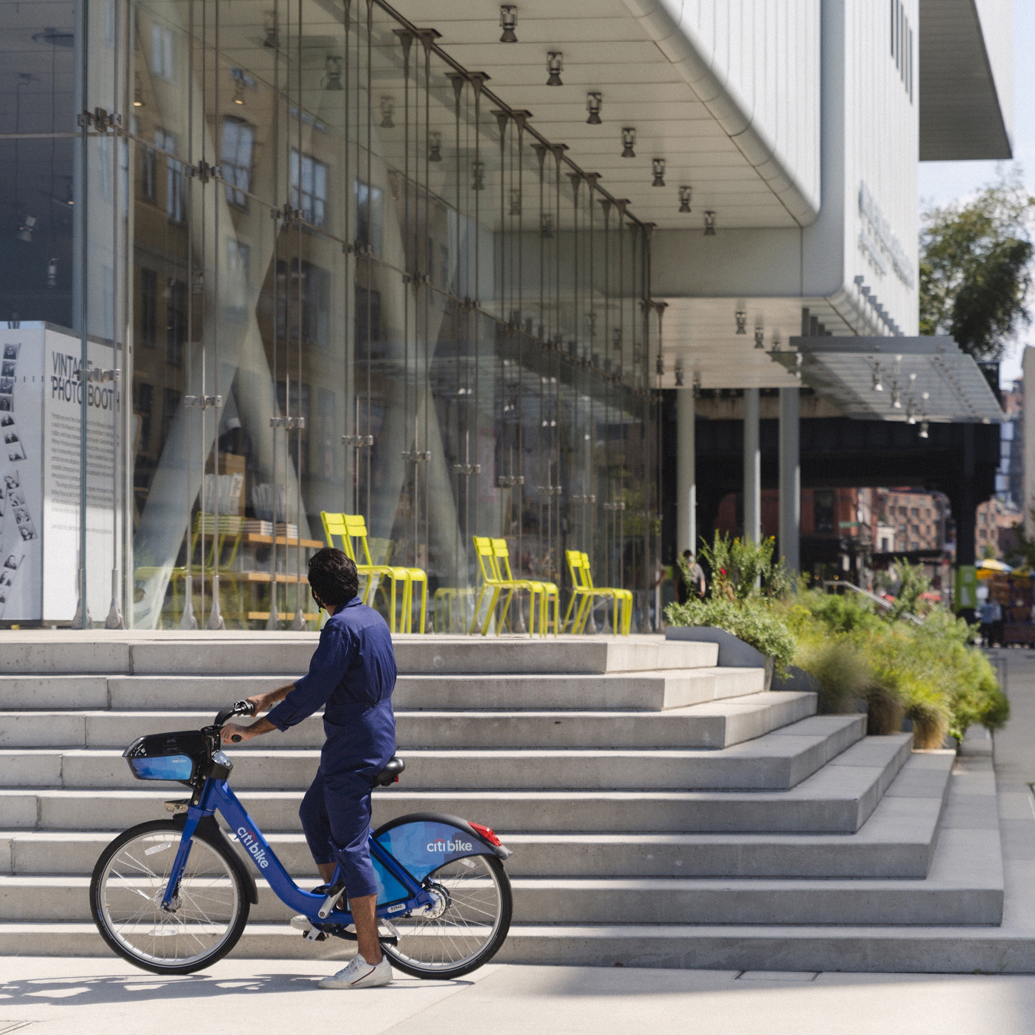 A person on a bike stands outside the Whitney Museum looking towards the glass lobby.